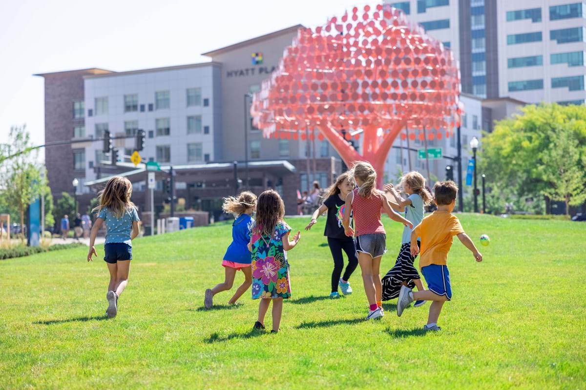 Children playing on the grass near a pink tree sculpture in Cherie Buckner Webb Park in downtown Boise.